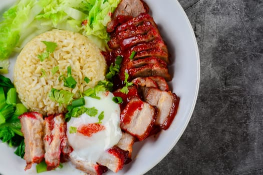 Barbecued red pork and crispy pork in red sauce, served with rice and vegetable on white plate.
