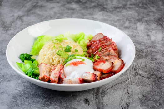 Barbecued red pork and crispy pork in red sauce, served with rice and vegetable on white plate.
