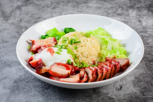 Barbecued red pork and crispy pork in red sauce, served with rice and vegetable on white plate.
