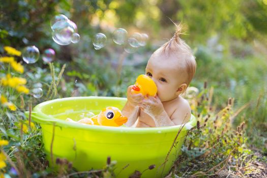 Cute little toddler boy in basin taking a bath with bubbles and duck toys outdoor