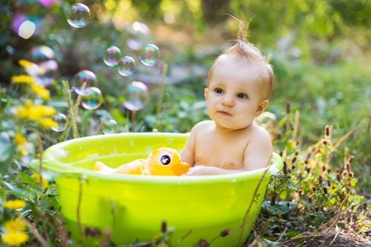Cute little toddler boy in basin taking a bath with bubbles and duck toys outdoor