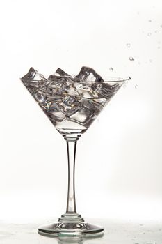 Glass, crystals of ice and pouring water on isolated studio background