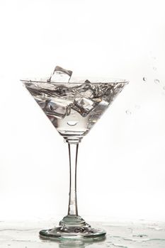 Glass, crystals of ice and pouring water on isolated studio background