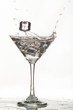 Glass, crystals of ice and pouring water on isolated studio background