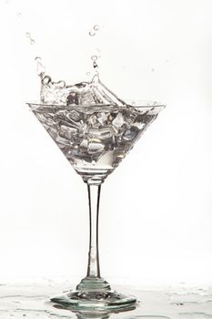 Glass, crystals of ice and pouring water on isolated studio background