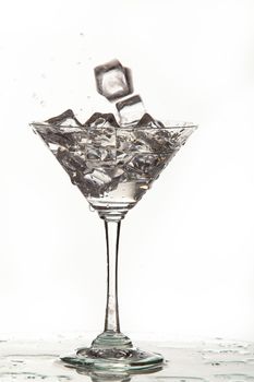 Glass, crystals of ice and pouring water on isolated studio background