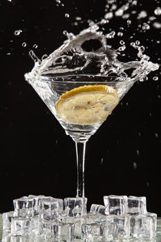 Glass of water, lemon and watersplashes on a black studio background