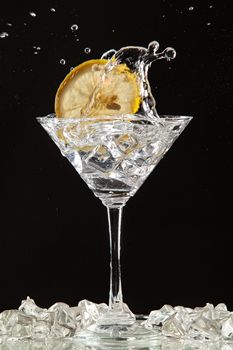 Glass of water, lemon and watersplashes on a black studio background