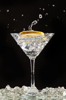 Glass of water, lemon and watersplashes on a black studio background