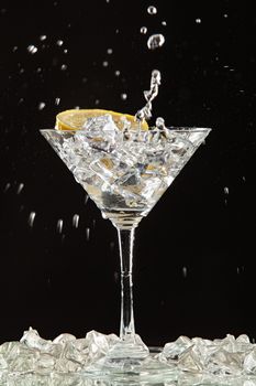 Glass of water, lemon and watersplashes on a black studio background