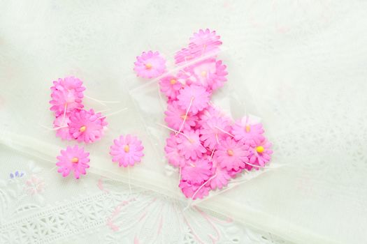 Handmade paper flowers on white fabric background, pink and yellow, decor for invitation card.
