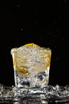 Glass of water, ice crystals and lemon on a black studio background