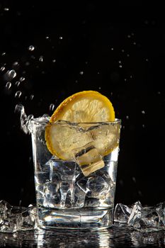 Glass of water, ice crystals and lemon on a black studio background