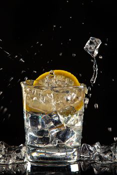 Glass of water, ice crystals and lemon on a black studio background