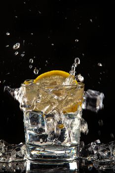Glass of water, ice crystals and lemon on a black studio background