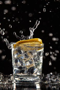 Glass of water, ice crystals and lemon on a black studio background