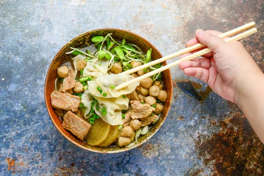 Wonton soup with meat balls, spring onion served in a big brown bowl, selective focus
