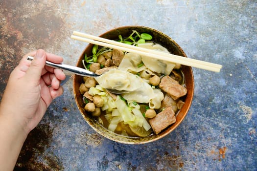 Wonton soup with meat balls, spring onion served in a big brown bowl, selective focus
