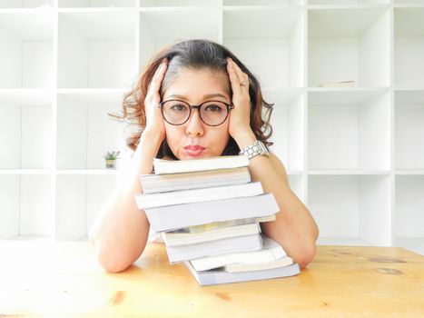 Beautiful women in glasses crushed on the table by a lot of books, very stressed of the study.
