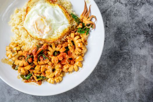 Spicy stir fried squid with basil leaves and chili, Sunny side up egg, served with brown rice. Hot and spicy dish.