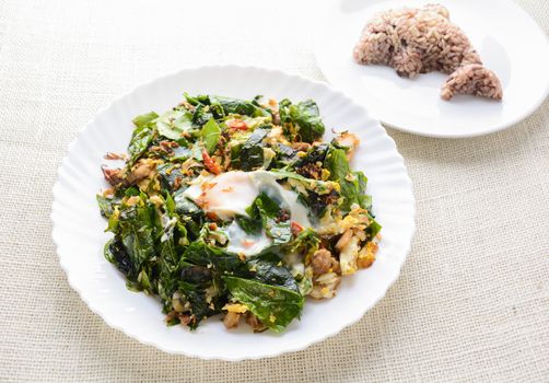 A white plate of delicious Stir-Fried Baegu Leaves or Melinjo with Eggs, served with steamed rice.