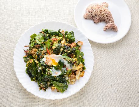 A white plate of delicious Stir-Fried Baegu Leaves or Melinjo with Eggs, served with steamed rice.