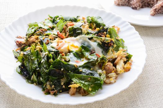 A white plate of delicious Stir-Fried Baegu Leaves or Melinjo with Eggs, served with steamed rice.