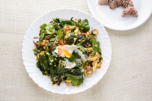 A white plate of delicious Stir-Fried Baegu Leaves or Melinjo with Eggs, served with steamed rice.