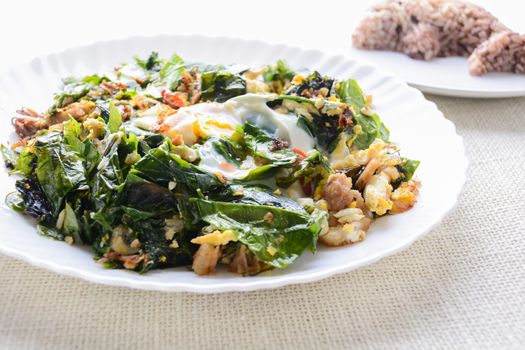 A white plate of delicious Stir-Fried Baegu Leaves or Melinjo with Eggs, served with steamed rice.