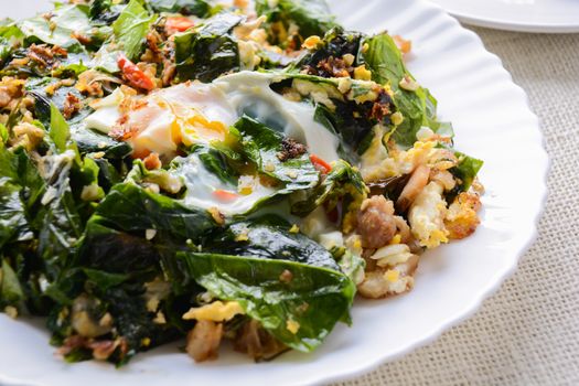 A white plate of delicious Stir-Fried Baegu Leaves or Melinjo with Eggs, served with steamed rice.