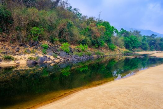 Landscape of sandy beach and water hole beside rocky cliff and reflection, copy space