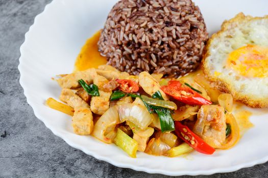 Stir fry chicken sweet onion and peppers, served with brown rice and fried egg on white plate
