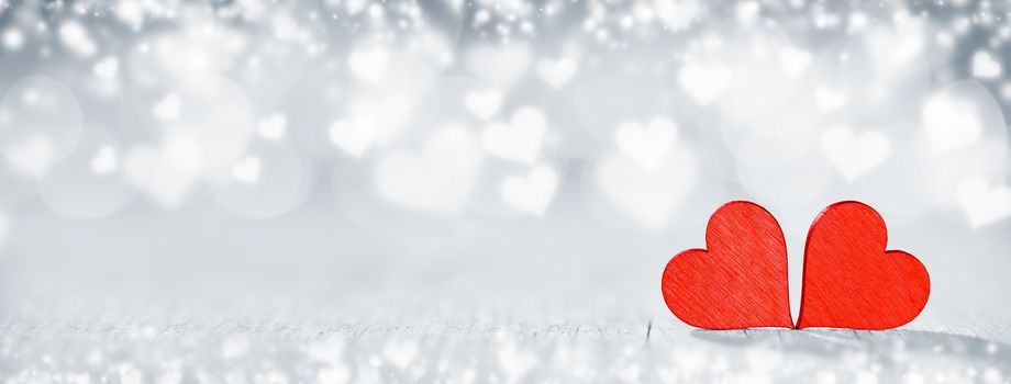Two wooden hearts on silver glowing bokeh hearts background for Valentines day