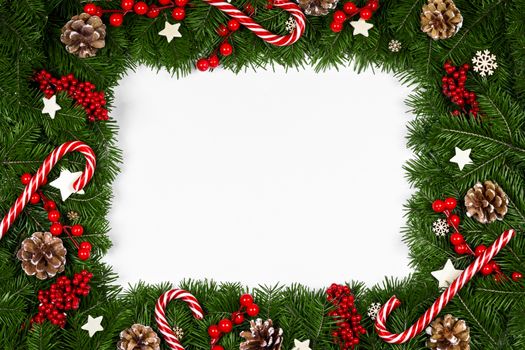 Christmas Border frame of tree branches around white background with copy space isolated, red decor, berries, stars, cones, candy canes