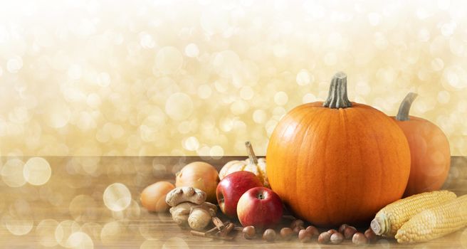 Autumn harvest still life with pumpkins, apples, hazelnut, corn on wooden background with copy space for text, golden glitter background