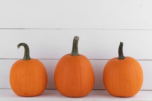 Three orange pumpkins on white wooden background, Halloween concept