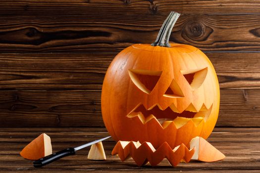 Carving of Halloween pumpkin in progress, pieces and cutting knife on wooden background
