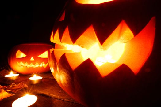 Three Halloween pumpkins head jack o lantern and candles on wooden table background