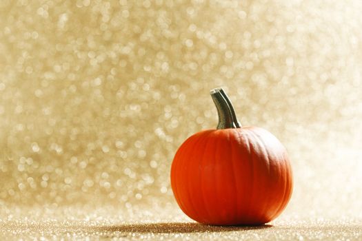 Pumpkin on golden glittery background with bokeh lights