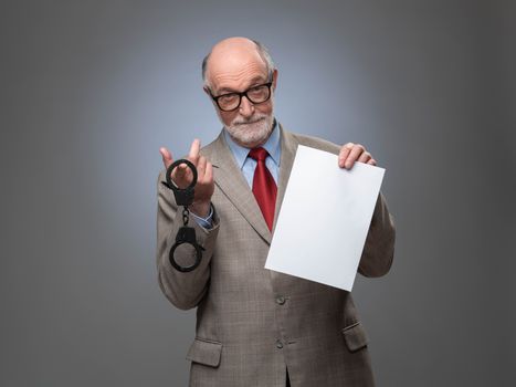 Senior business man with handcuffs and blank contract paper hints at danger of financial crimes