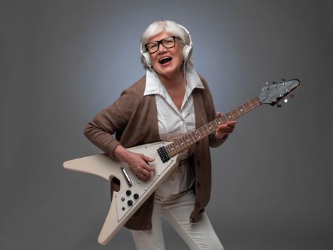 Happy funny senior woman playing electric guitar