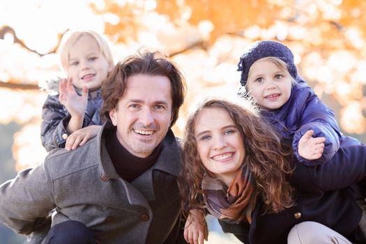 Happy smiling family of parents and children having fun hugging in autumn park