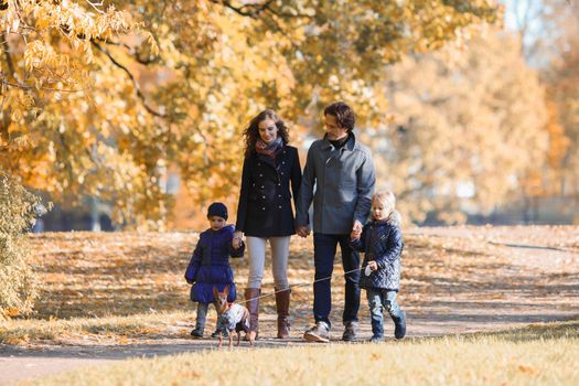 Happy smiling family of parents and children walking together holding hands in autumn park
