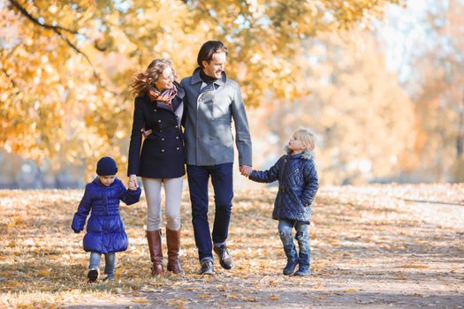 Happy smiling family of parents and children walking together holding hands in autumn park