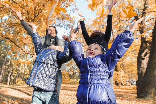 Happy smiling family of parents and children playing throwing leaves in autumn park