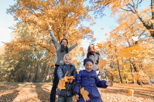 Happy smiling family of parents and children playing throwing leaves in autumn park