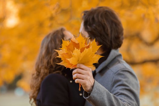 love, relationship, family and people concept - couple with maple leaves kissing in autumn park