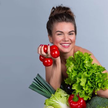 Portrait of young beautiful woman with bare shoulders holding many vegetables