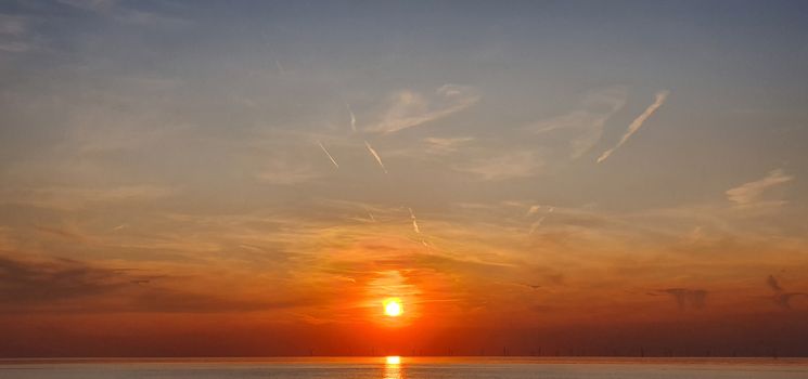 Windmills in the North Sea during fiery orange sunset.