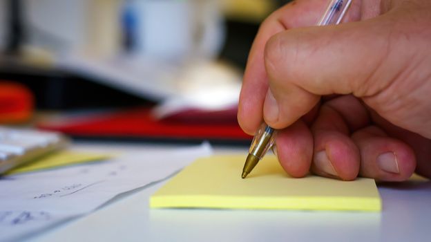 Male hand writing with a pen on a yellow sheet